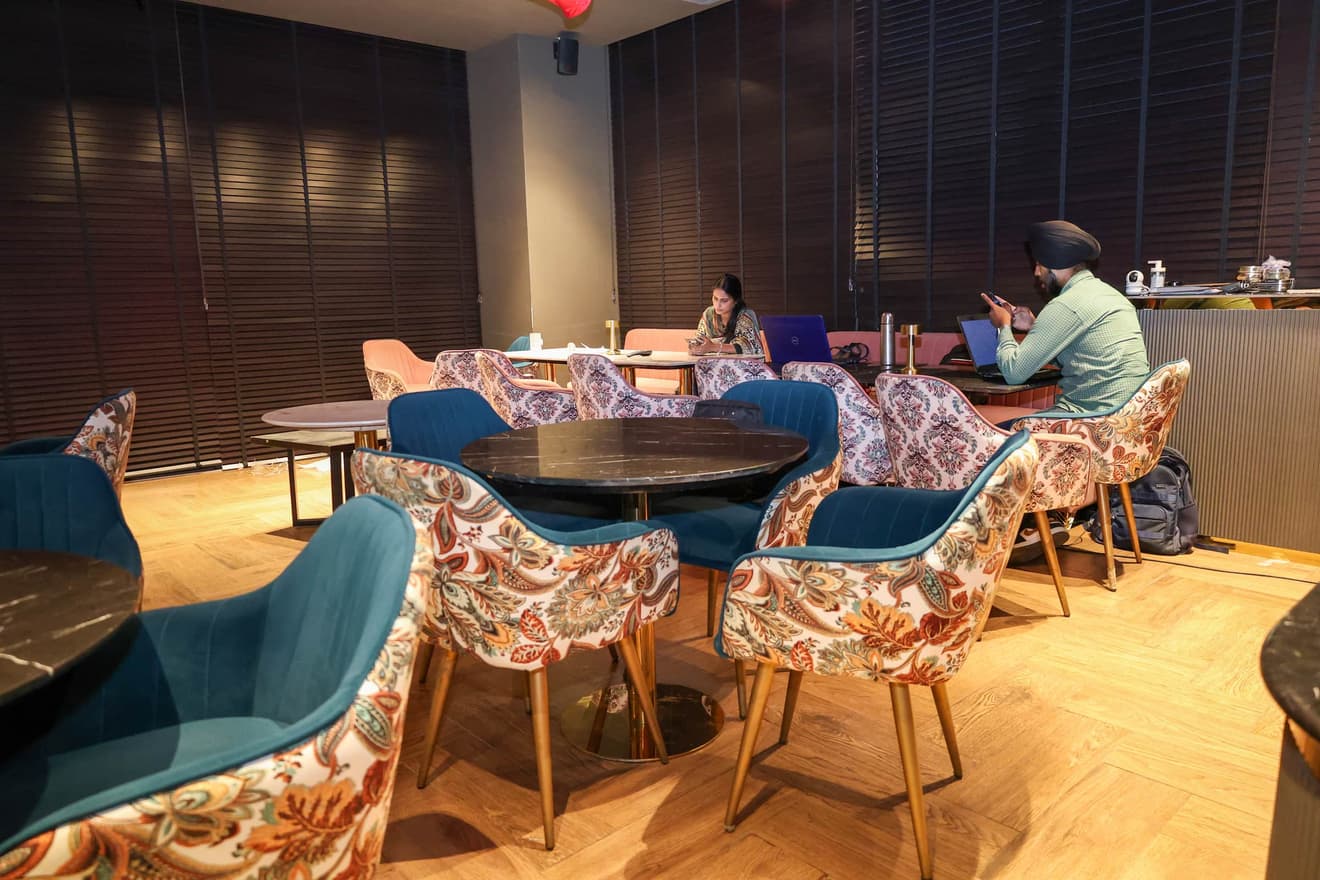 Warmly lit lounge seating area with teal velvet and floral-print chairs around marble bistro tables.