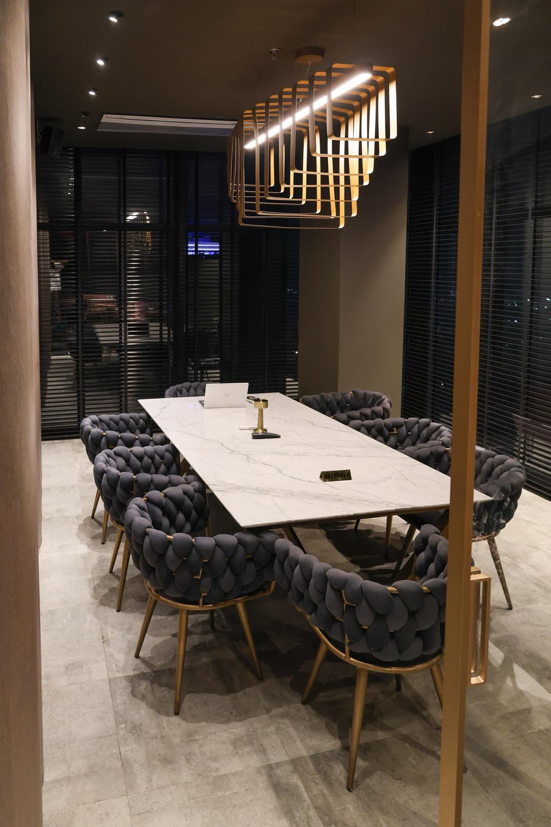 Private dining table with woven charcoal chairs under a geometric brass pendant light.