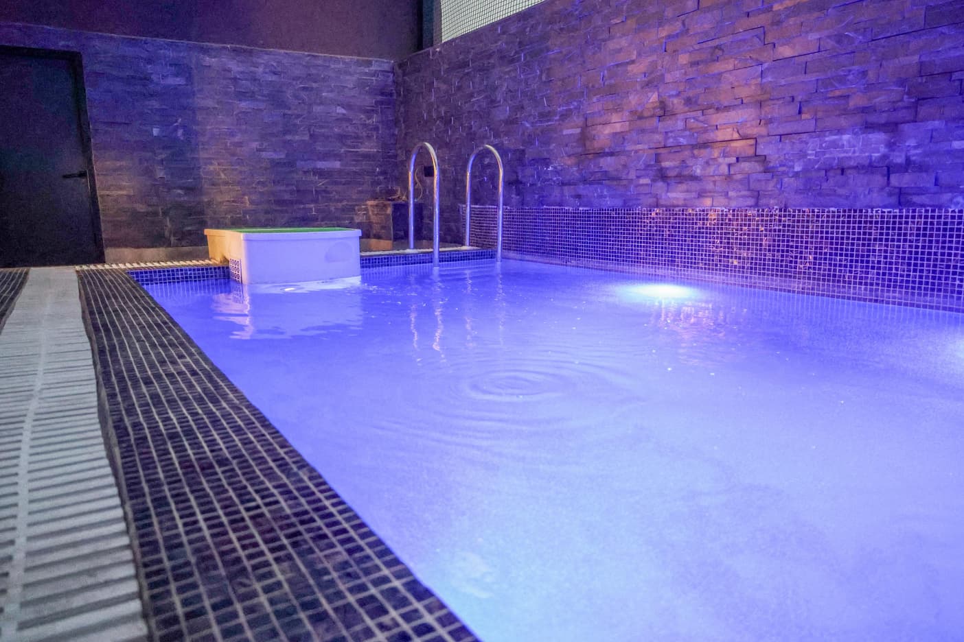 Aquila Grand Suite indoor plunge pool, lit in blue with stone-textured walls.